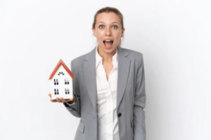 Young real estate agent woman holding a home model isolated on white background screaming