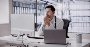 Young doctor sits at desk looking at patient medical records on computer