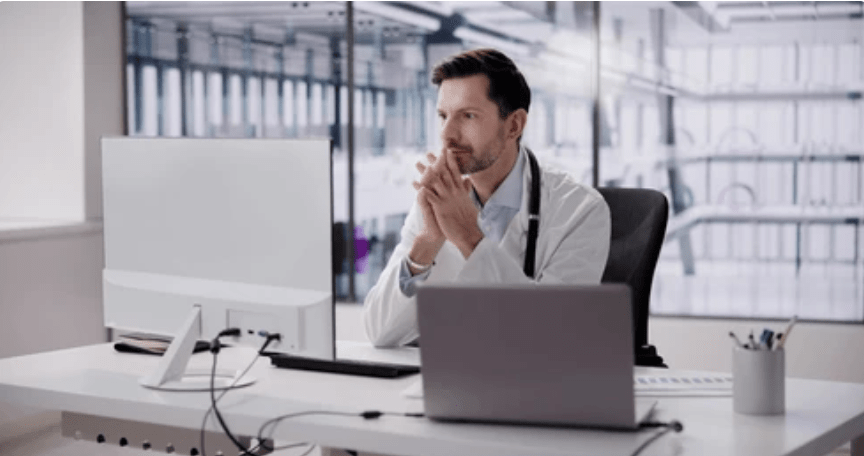 Young doctor sits at desk looking at patient medical records on computer