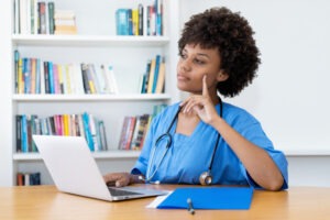 Concerned female nurse in scrubs at laptop, wondering how to appeal a suspended nursing license in Texas