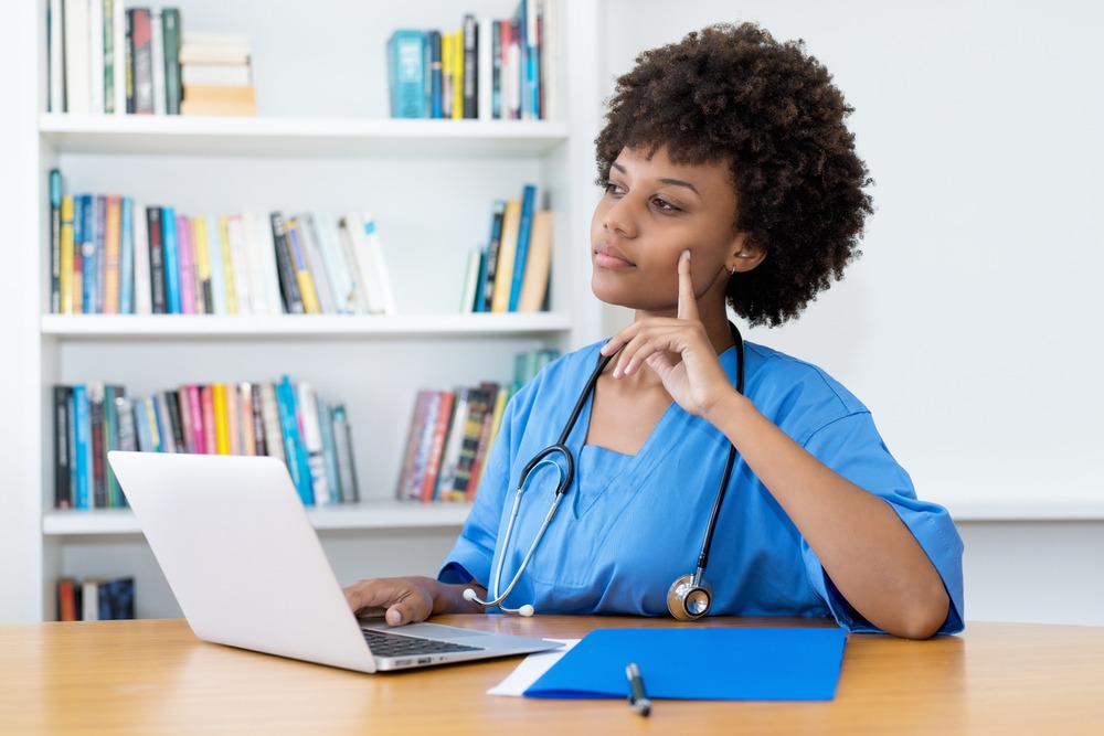 Concerned female nurse in scrubs at laptop, wondering how to appeal a suspended nursing license in Texas