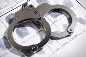 A pair of handcuffs and its key rest atop a fingerprint identification booking card, inferring crime